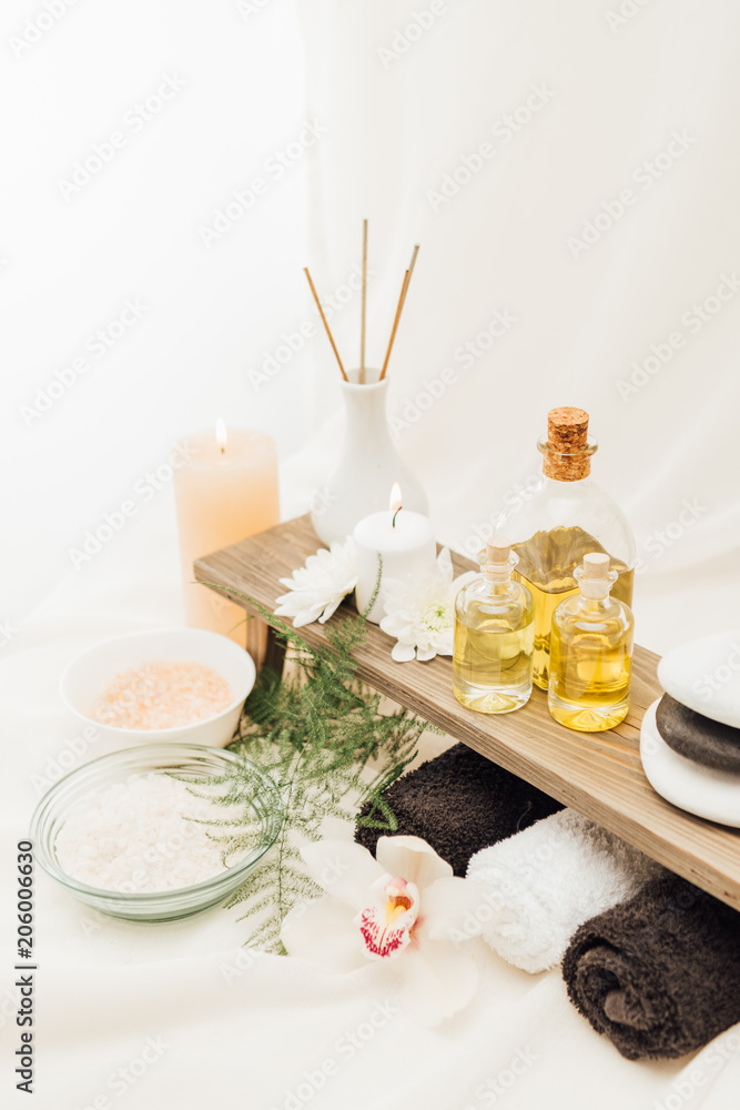 close up view of arrangement of spa treatment accessories with towels, oil and salt on white background close up view of arrangement of spa treatment accessories with towels, oil and salt on white background