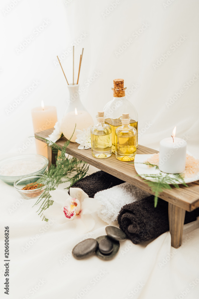 close up view of arrangement of spa treatment accessories with essential oil, salt and candle on white background