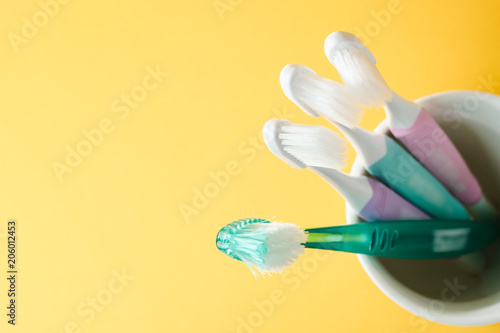 Close-up three white plastic toothbrushes and old green toothbrush in white mug on yellow background  Selected focus