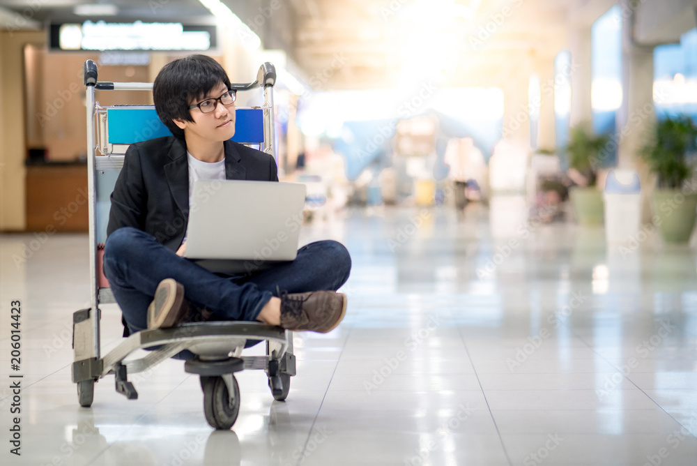 Young asian man working on airport trolley with his laptop computer during waiting for a connecting flight, freelance lifestyle and digital nomad concepts Young asian man working on airport trolley with his laptop computer during waiting for a connecting flight, freelance lifestyle and digital nomad concepts