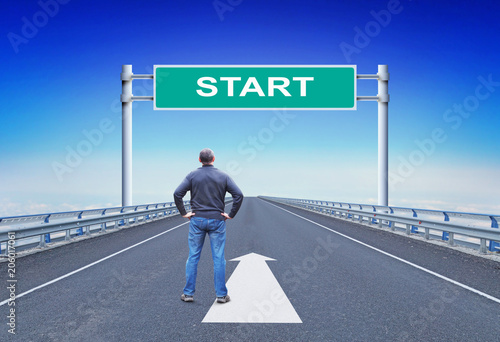 Man stands on a highway in front of road sign with text Start. Concept of beginning and changes