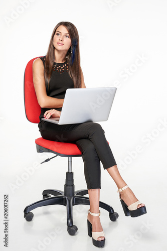 Business woman sitting on office chair working with laptop thinking looking away at blank copy space, full length portrait