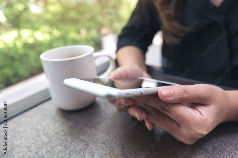 Closeup image of a woman using and looking at smart phone with coffee cup in cafe