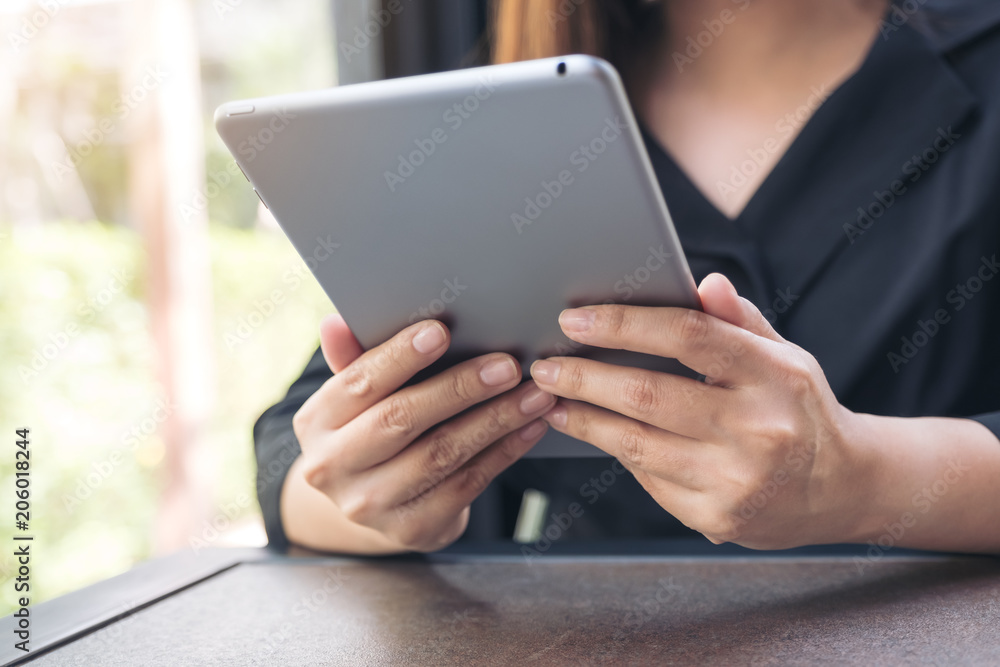 Closeup image of a woman holding and using tablet pc in modern cafe