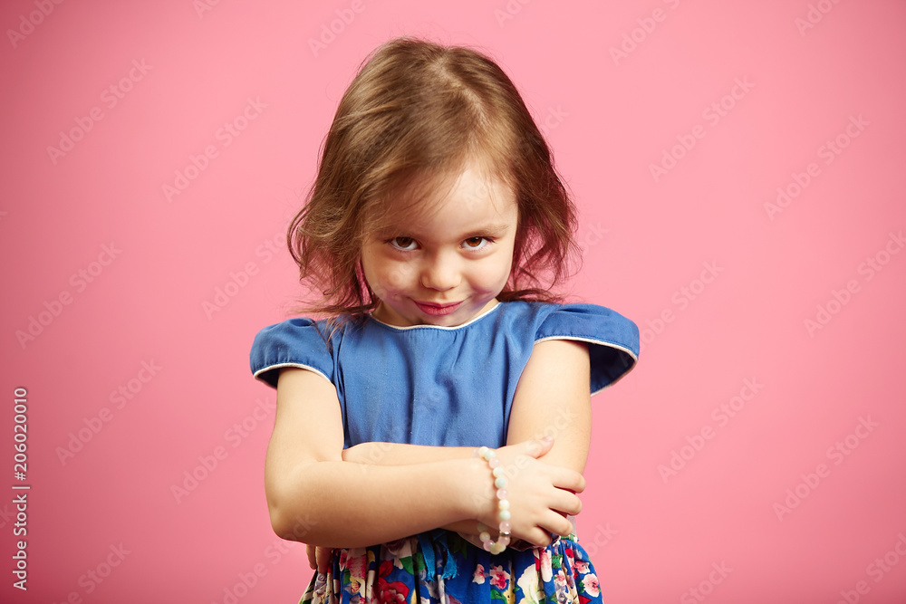 Offended little girl looks at the camera with a glance, expresses resentment or anger, demonstrates her character, portrait of frustrated child on pink background. Offended little girl looks at the camera with a glance, expresses resentment or anger, demonstrates her character, portrait of frustrated child on pink background.