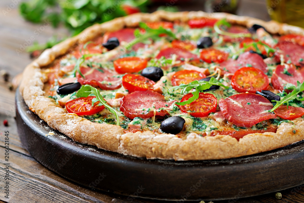 Pizza with salami, tomatoes, olives and cheese on a dough with whole wheat flour. Italian food.