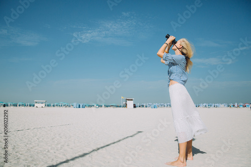 Beautiful natural blonde woman looking through binoculars against blue sky
