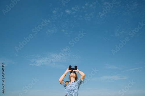 Beautiful natural blonde woman looking through binoculars against blue sky