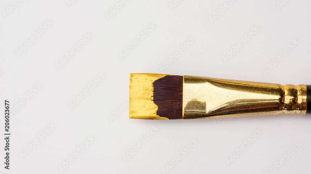 Obraz premium Paintbrush and gold colored poster on a white background.