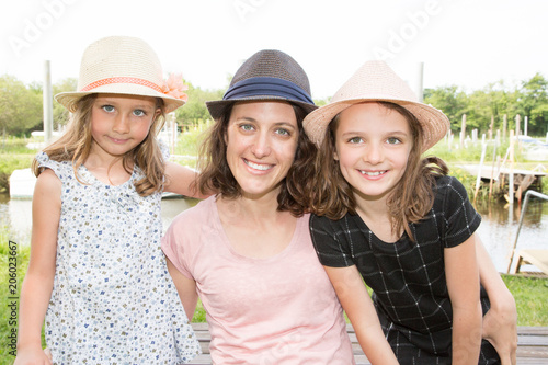 smile mother outdoor nportrait with two girls daughter with straw hat near lake river in spring photo