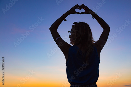 Silhouette of a girl holding heart - shape sign with her hands.