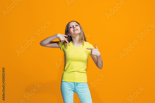 The happy teen girl standing and smiling against orange background. © master1305