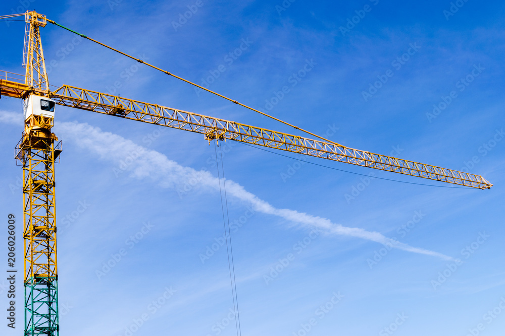 Construction crane tower on blue sky background. Crane and building working progress. Yellow lifting faucet. Empty Space for text. Construction concept. Site. New buildings with a crane. Tower crane