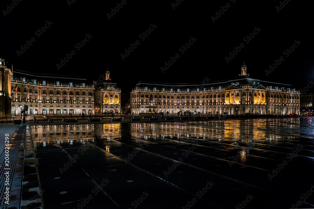 Bordeaux, France, 10 may 2018 - Tourists visiting the Place de la Bourse at night seen from the boulevard with in front the mirror fountain: 'Mirroir d'eau'