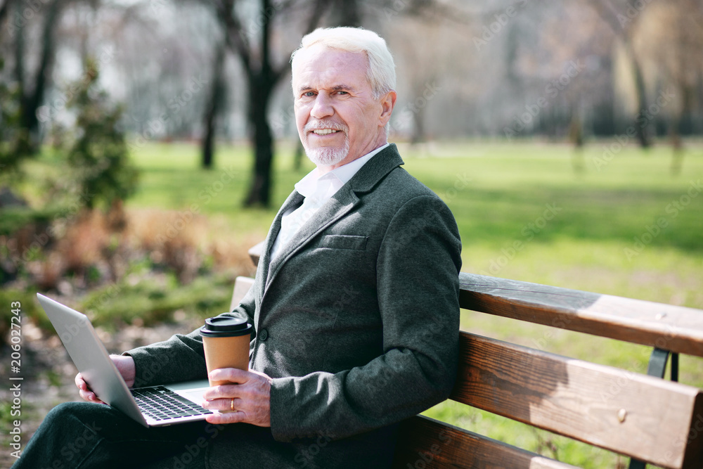Warm weather. Enthusiastic mature businessman using laptop while drinking coffee Warm weather. Enthusiastic mature businessman using laptop while drinking coffee