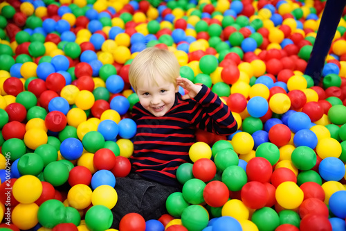 Happy little boy having fun in ball pit with colorful balls