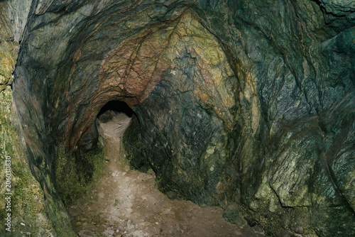 Beautiful cave. View from inside dark dungeon. Textured walls of cave. Background image of underground tunnel. Dampness inside cave. Light at end of tunnel.