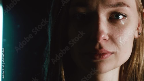 A sad woman is crying. The girl is depressed. A woman in a dark room. Tears roll down her cheeks.