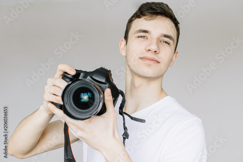 A young man holds a photo camera in his hand and looks straight. Іsolated gray background photo
