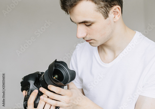 A young man holds a photo camera in his hand and looks at the lens in the dust, a dirty lens. Іsolated gray background photo