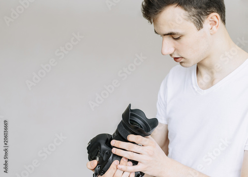 A young man holds a photo camera and looks at it. Іsolated gray background photo