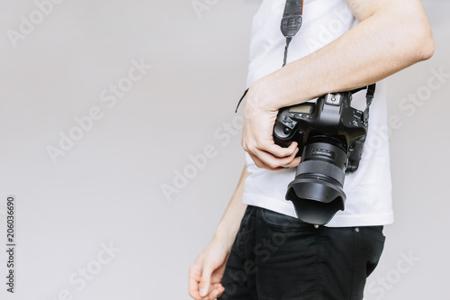 Young man carries a photo camera on his shoulder. Іsolated gray background photo
