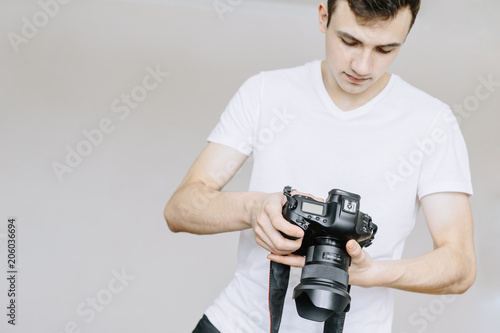 A young man holds a photo camera in his hand and looks at the photo on the photo camera photo