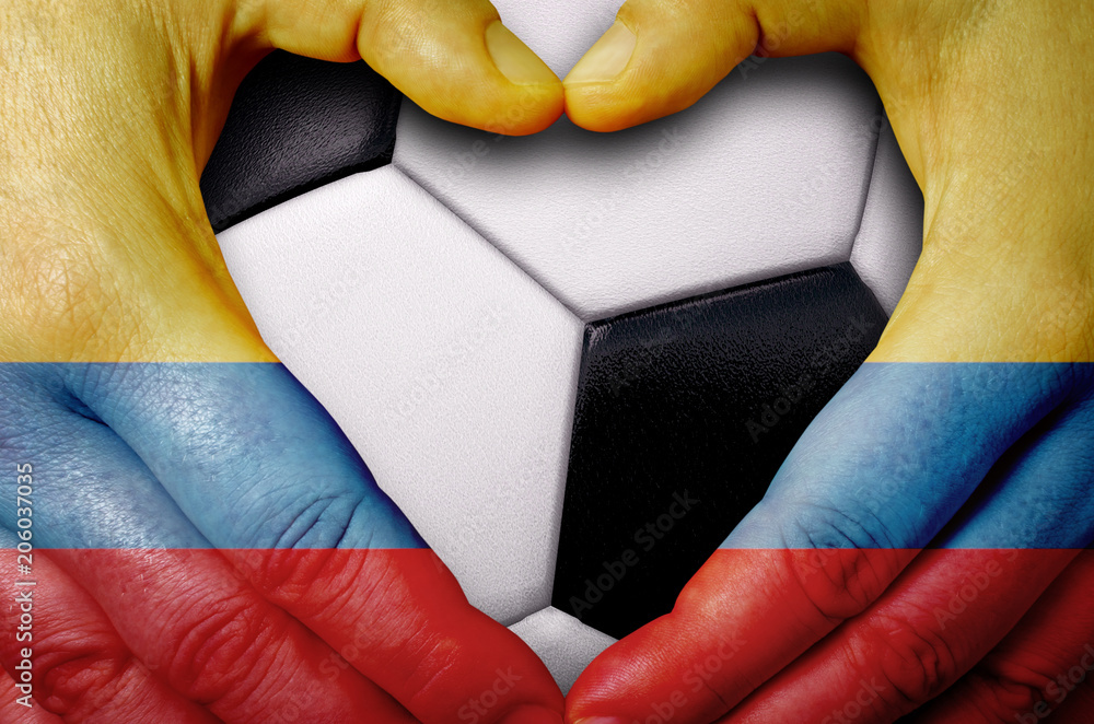 Naklejka premium Hands painted with a Colombia flag forming a heart over soccer ball background