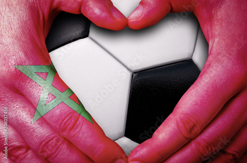 Hands painted with a Morroco flag forming a heart over soccer ball background