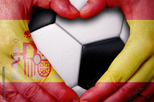 Hands painted with a Spain flag forming a heart over soccer ball background