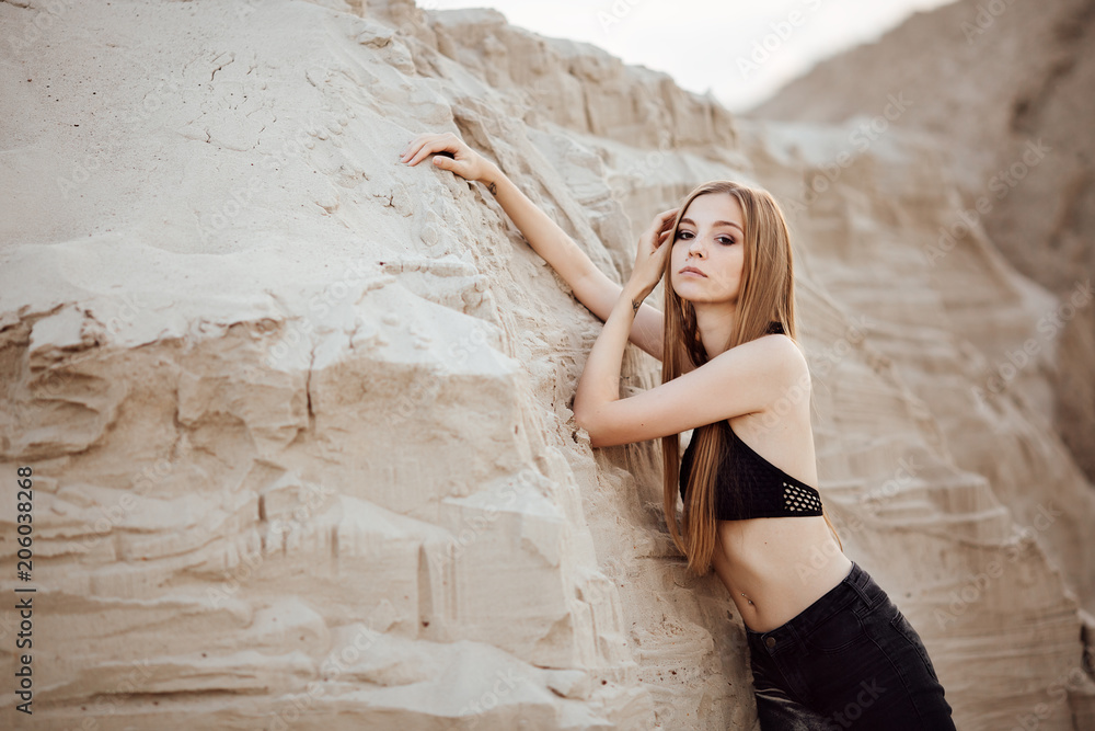 Portrait of a beautiful girl with long hair on the sands in the desert at sunset. Girl model in black jeans and top