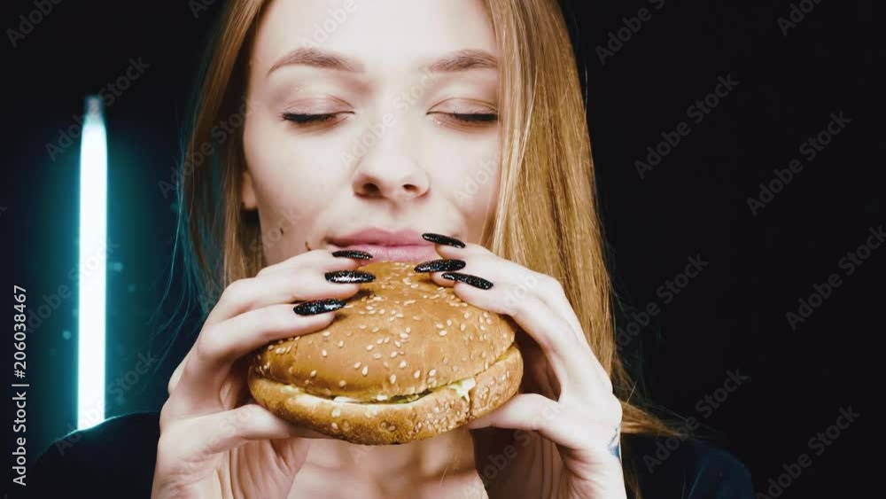 Slender girl holding a hamburger. She enjoys his scent. Delicious fast food. Slender girl holding a hamburger. She enjoys his scent. Delicious fast food.