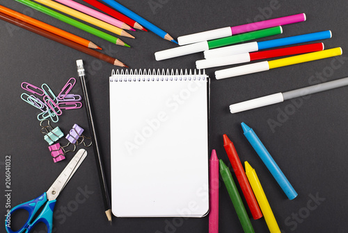 Colored pencils, stationery, and notebook on black background. Back to school concept.