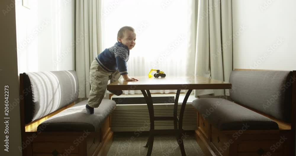 Toddler boy climbs onto table to grab toy tractor Toddler boy climbs onto table to grab toy tractor