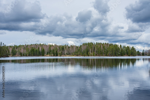 Forest on the shore of lake with cloudy sky above, reflected in the water. Taken along the Bergslagsleden hiking trail, in nature reserve Ånnaboda in central Sweden.