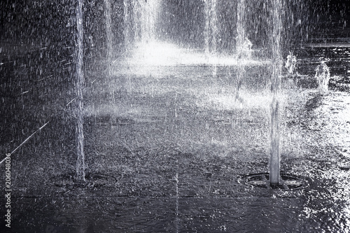 Quadro su tela Water jets of a modern fountain on a stone pavement - toned image