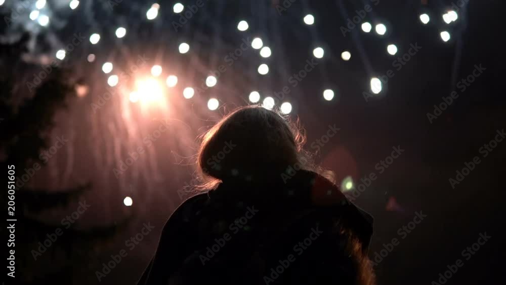 The girl takes pictures of fireworks on a mobile phone. Silhouette on the background of the sky illuminated by lights. The girl takes pictures of fireworks on a mobile phone. Silhouette on the background of the sky illuminated by lights.