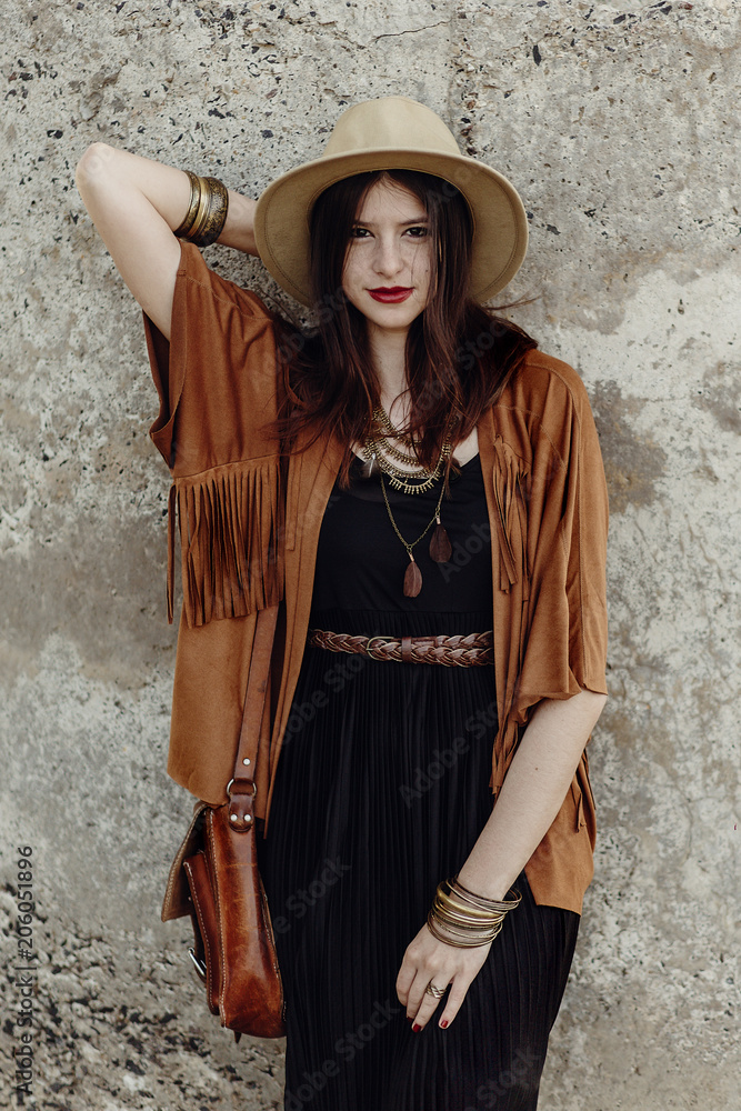 stylish boho woman with jewelry posing at rock wall. beautiful hipster  gypsy dressed girl with hat and fringe poncho with sensual look. young girl  traveler. fashionable hippie outfit. summer vacation Stock Photo