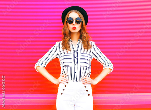 Glamour woman wearing a black hat sunglasses white pants over colorful pink  background