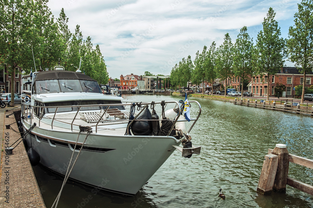 Boat moored on wide canal margin under sunny blue sky in the City Center of Weesp. Quiet and pleasant village full of canals and green near Amsterdam. Northern Netherlands. Boat moored on wide canal margin under sunny blue sky in the City Center of Weesp. Quiet and pleasant village full of canals and green near Amsterdam. Northern Netherlands.