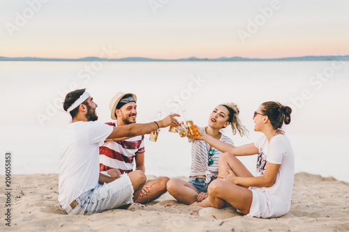 Group of happy young people sitting together at the beach talking and drinking beers 