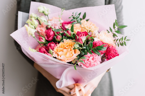 Fototapeta Naklejka Na Ścianę i Meble -  Very nice young woman holding a colourful fresh blossoming flower bouquet of different sorts of roses, carnations, eustoma, peonies on the grey wall background