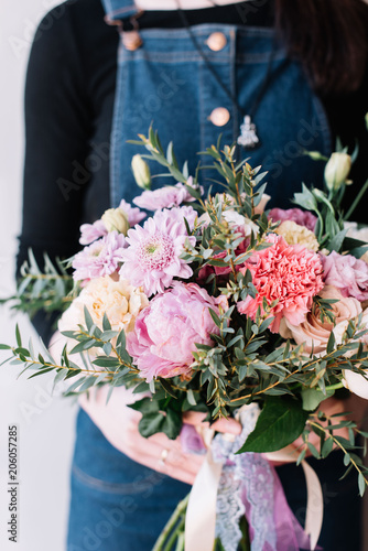 Very nice florist woman holding a beautiful colourful blossoming flower bouquet of peony  carnations  roses  eustoma  chrysanthemums  pistachio leaves on the grey wall background