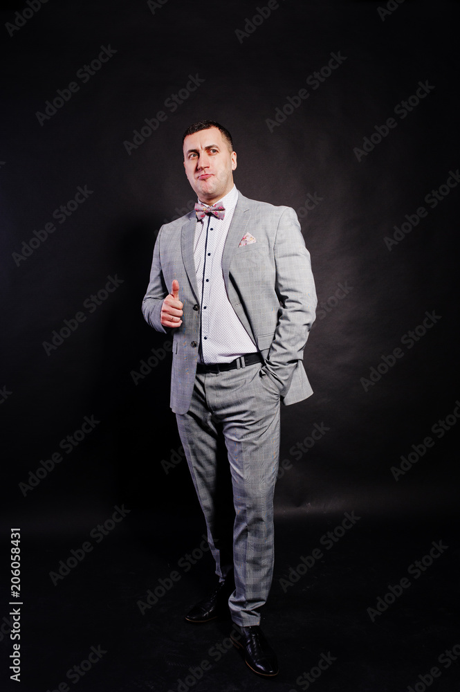 Studio portrait of man in gray suit and bow tie showing thumb up against black background. Studio portrait of man in gray suit and bow tie showing thumb up against black background.