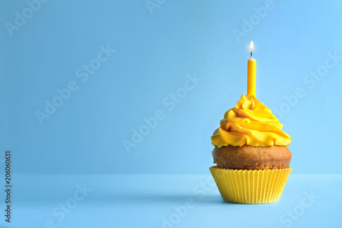 Delicious birthday cupcake with candle on color background