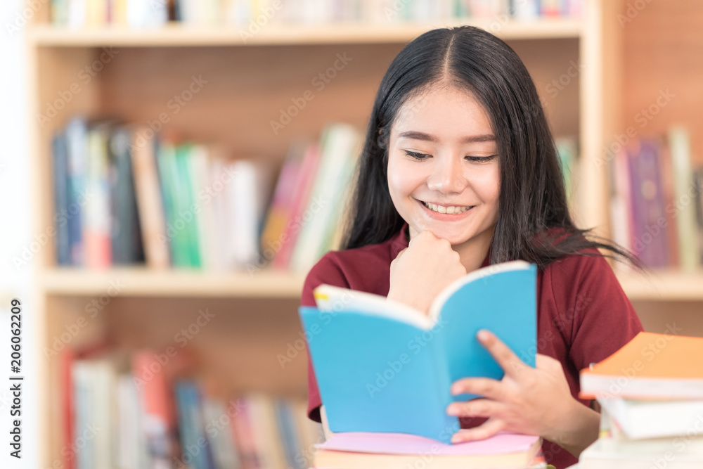 Cheerful girl sitting by wooden table and Reading book in library. Cheerful girl sitting by wooden table and Reading book in library.