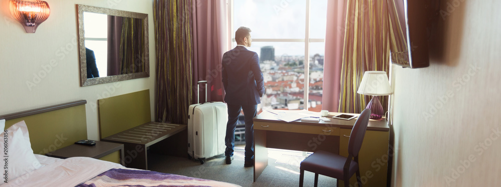 Young businessman with luggage in hotel room - obrazy, fototapety, plakaty 