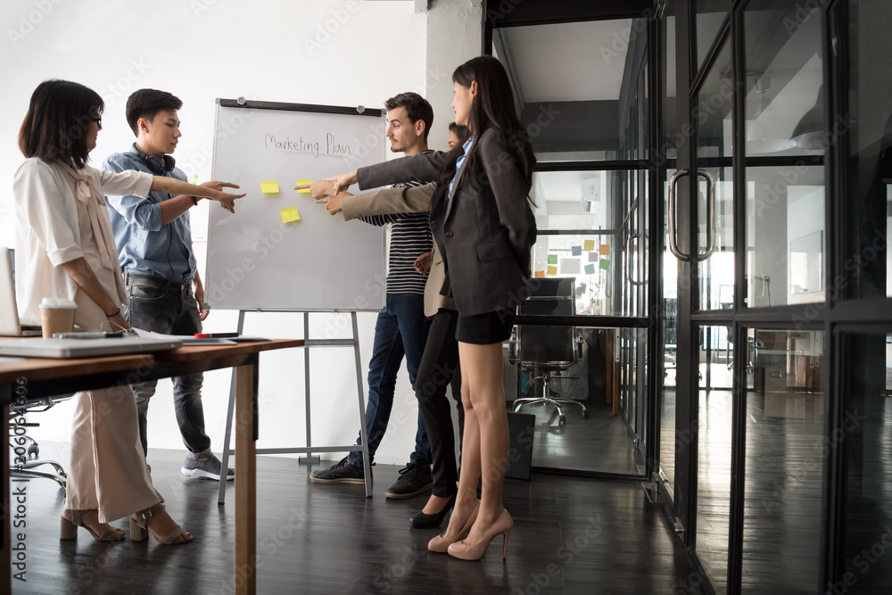 Group of young modern people in casual wear planning business strategy. Business team analyzing income charts and graphs. Setup studio shooting. selective focus at whiteboard.