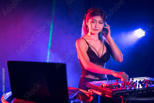 Portrait of active pretty young DJ woman playing music on laser lighting background.