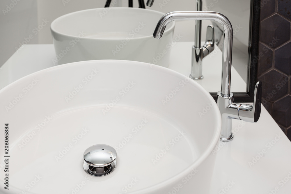 Fototapeta premium Element of bathroom interior with white sink and large mirror. New wash basin and black tile.